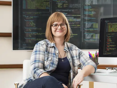 Kvinne smiler med skjermer rundt seg som viser kode