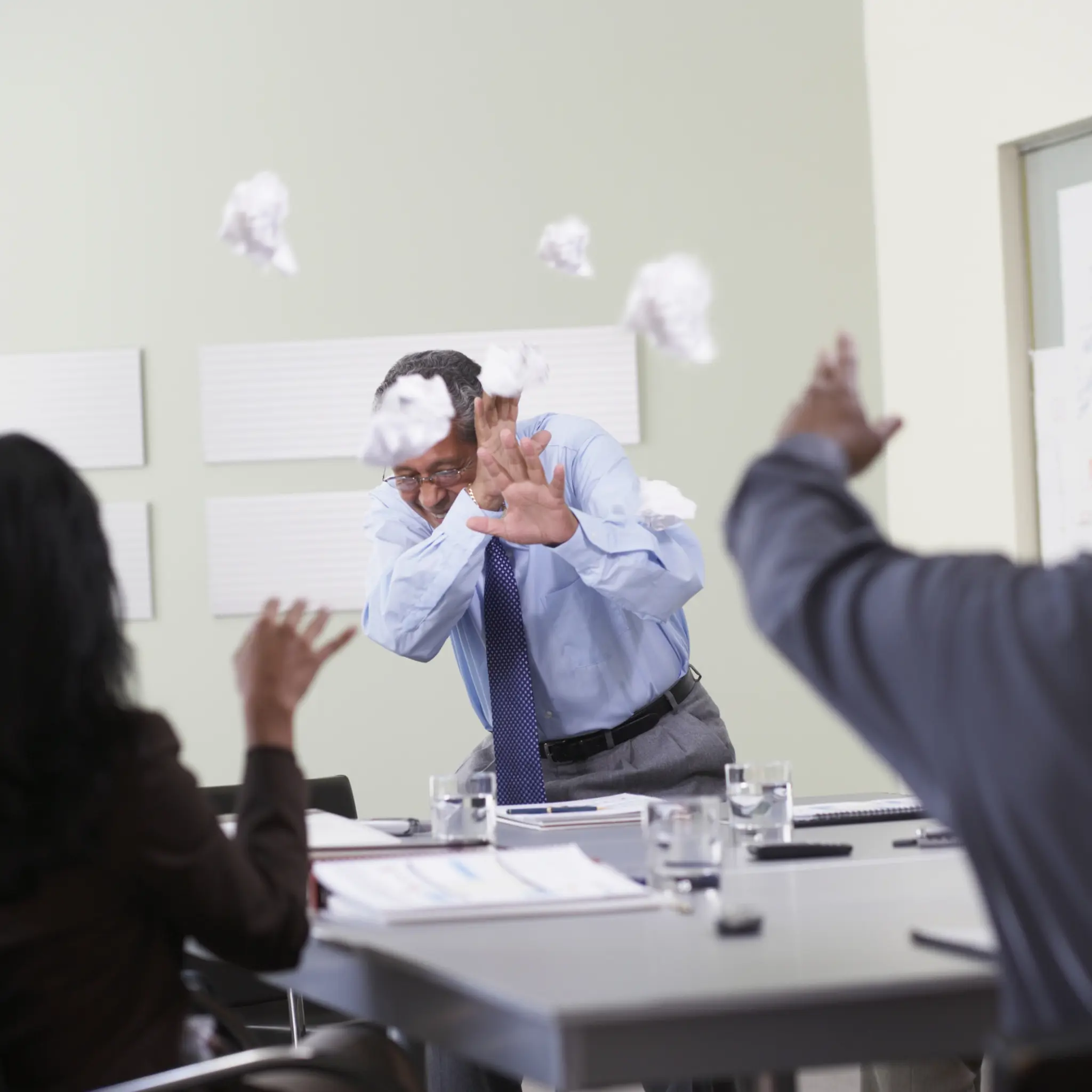 Illustrasjonsbilde av et møte i en bedrift hvor møtedeltakere kaster papir og søppel på møtelederen