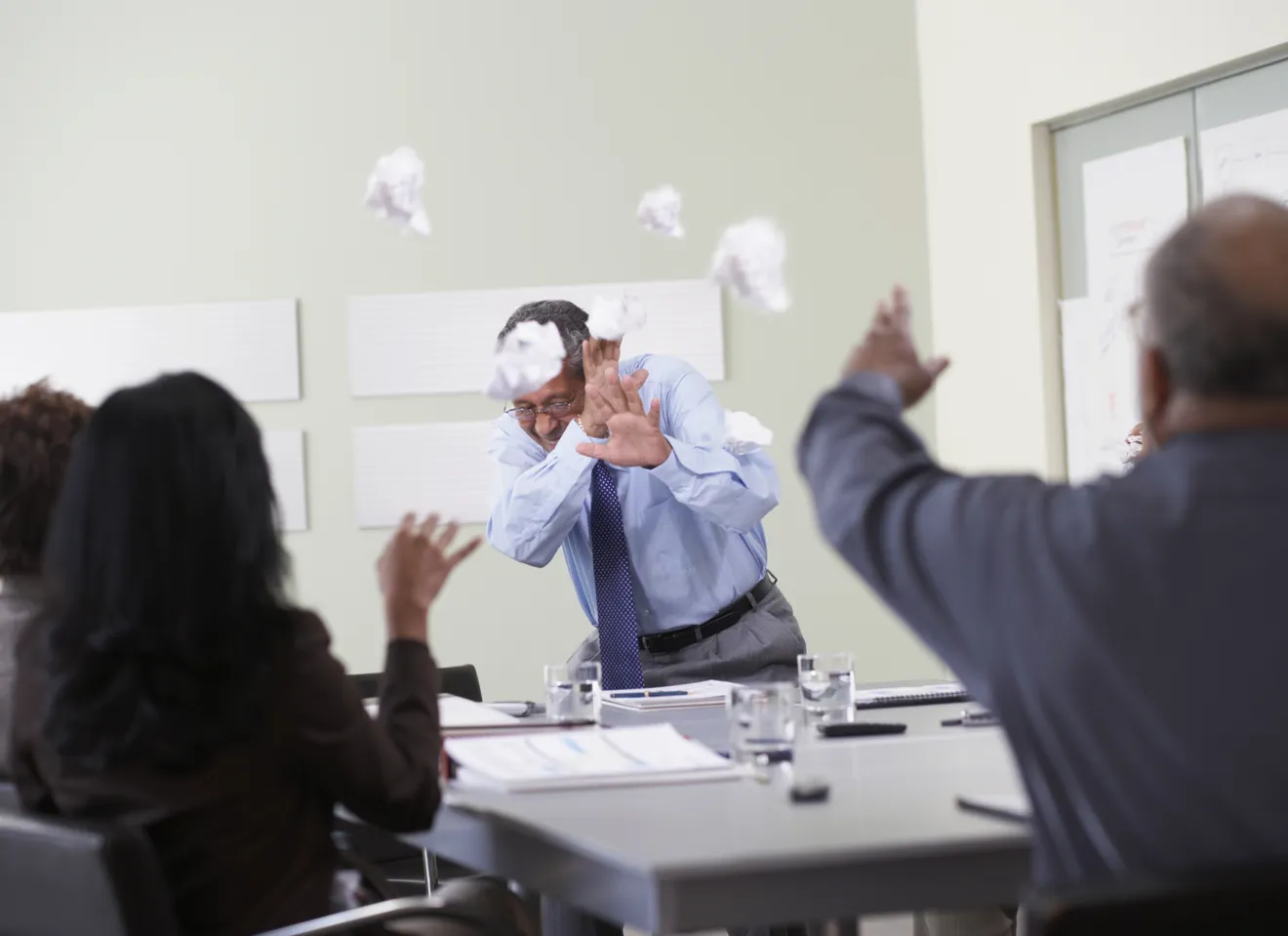 Illustrasjonsbilde av et møte i en bedrift hvor møtedeltakere kaster papir og søppel på møtelederen