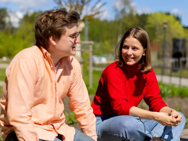 En kvinnelig og en mannlig student sitter i en park og snakker med hverandre