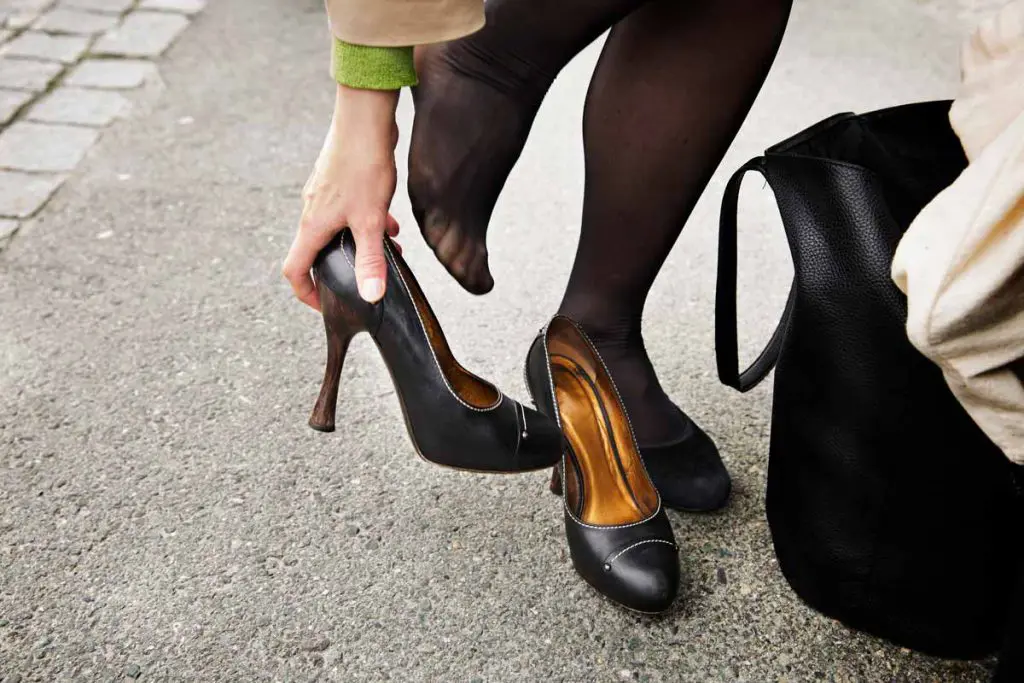 Nærbildet av føtter som tar på sorte sko med høye hæler 