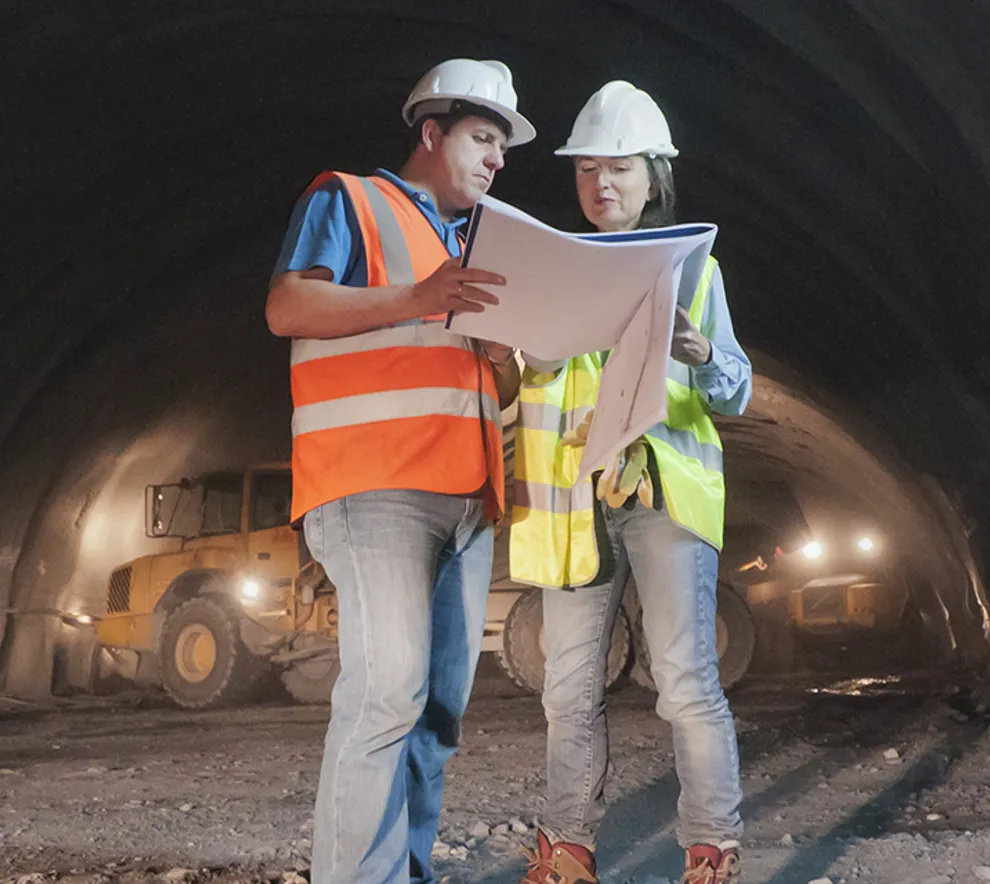 To arbeidere som studerer planer/skisser ved arbeid i en tunnel