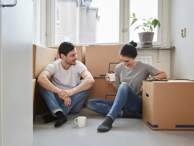 En ung mann og ung kvinne sitter blant pappesker i et tomt rom med dagslys