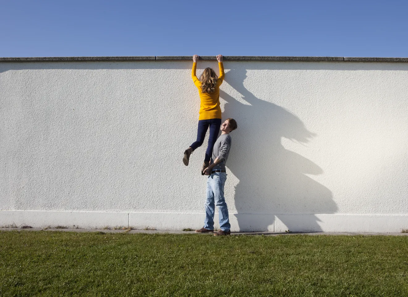 Illustrasjonsbilde av en ung mann som løfter opp en ung kvinne over en stor vegg