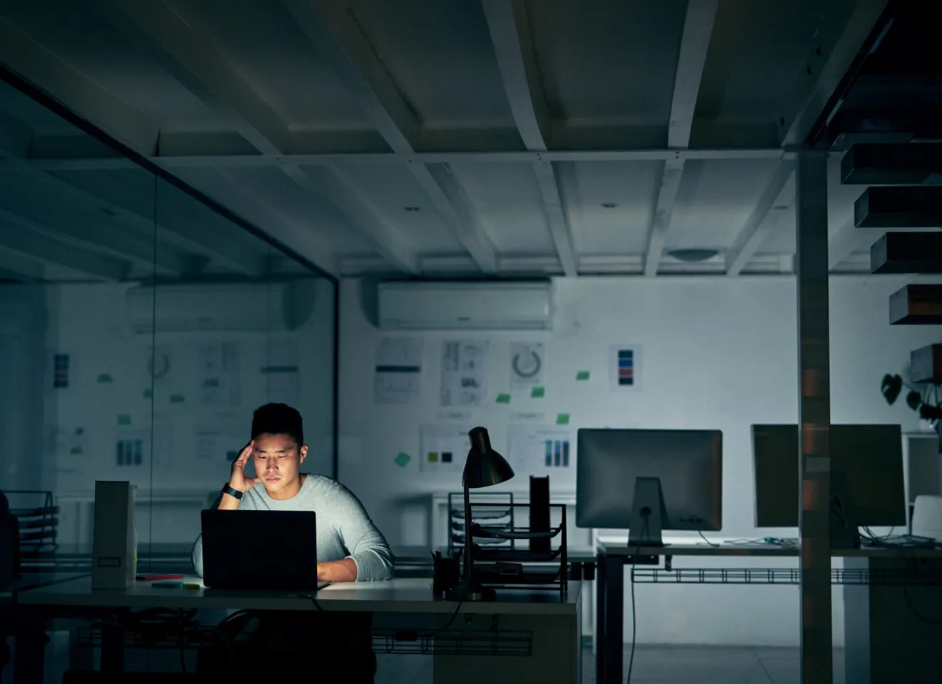 Person jobber overtid sent på kvelden i mørke kontorlokaler med lys fra dataskjermen. 
