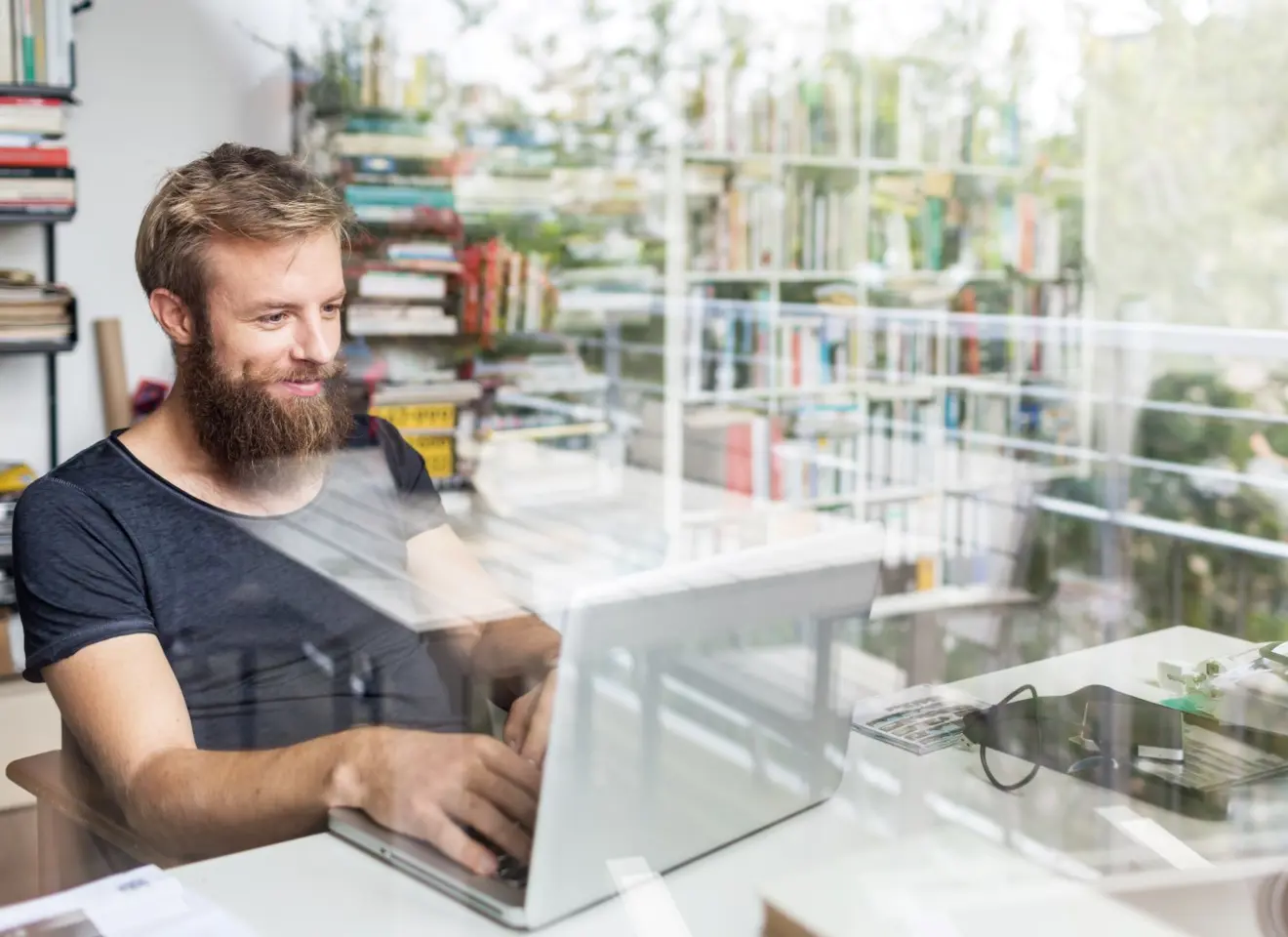 Ung mann med skjegg sitter foran laptop på hjemmekontor og smiler