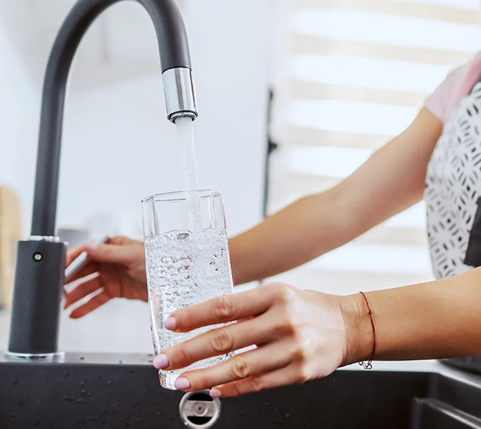 En person fyller et glass vann fra springen