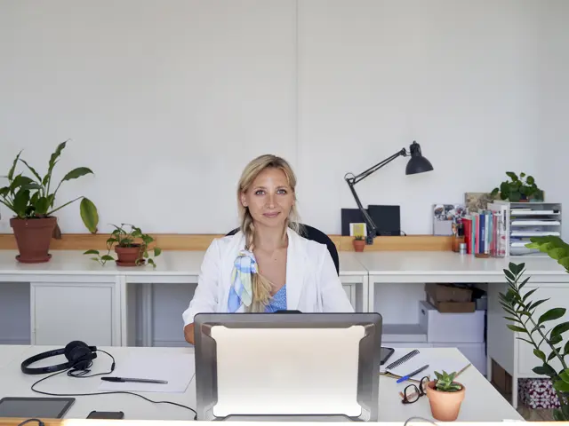 Illustrasjonsbilde av en ung kvinne som sitter på kontoret og smiler til kamera