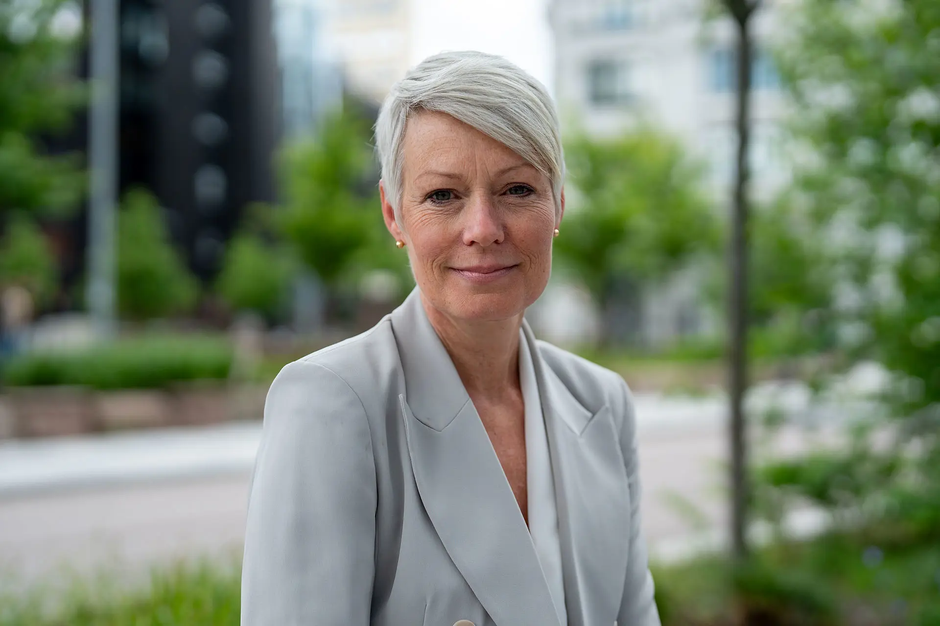 Line Henriette Holten, nøytralt ansiktsuttrykk, grå jakke, grønne blader i bakgrunnen
