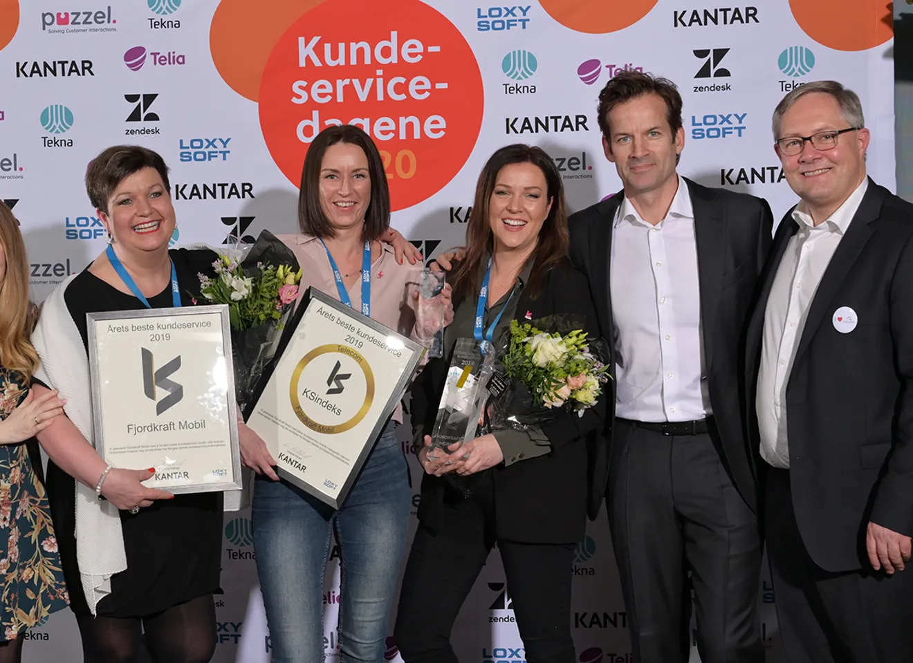 Ledelsen i Fjorkraft med diplom og blomster foran en Kundeservicedagene pressevegg