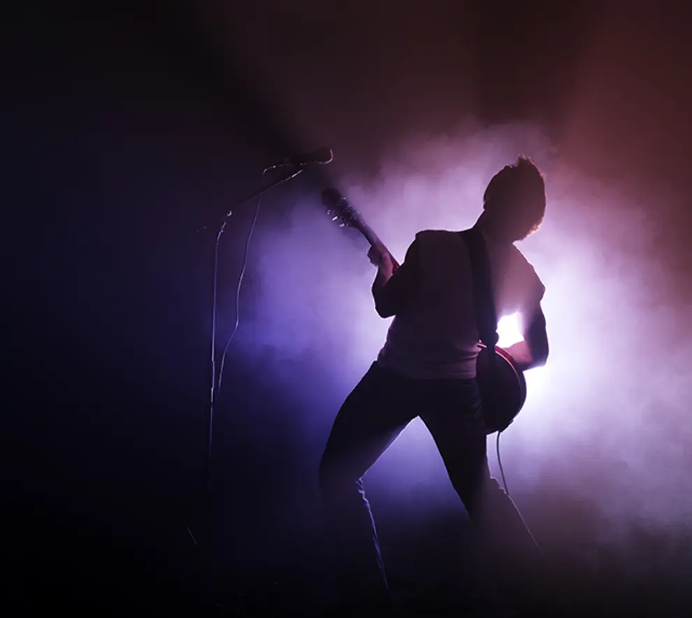 Silhuett av en mann som spiller gitar på en røyklagt scene