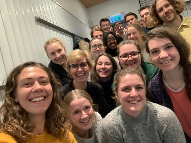 Gruppebilde av mange personer står tett sammen og smiler til kamera