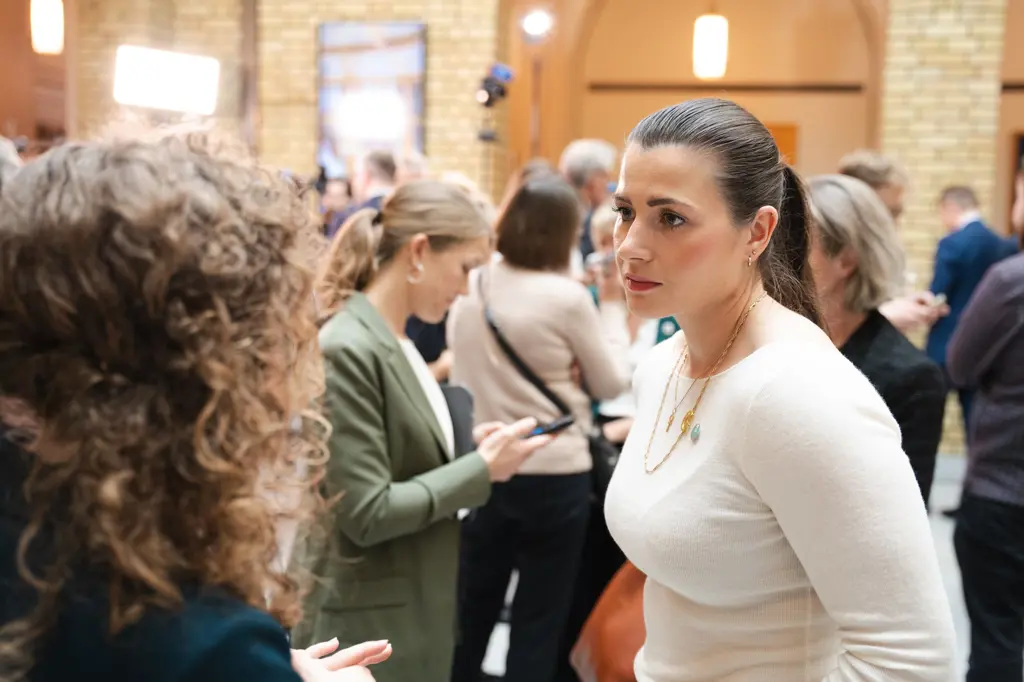 Elisabet Haugsbø hvit genser, alvorlig ansiktsuttrykk, i Vandrehallen på Stortinget, i samtale med andre personer 