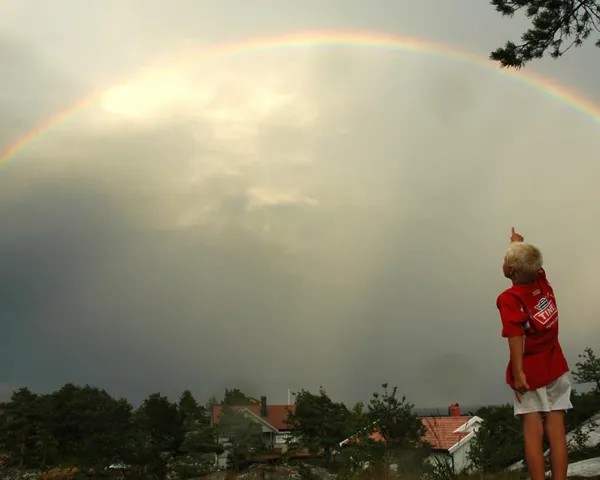 En ung gutt med blond hår peker opp til en stor regnbue