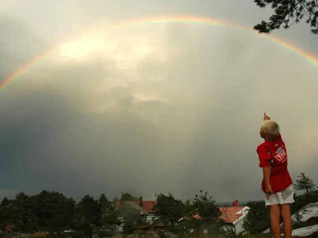 En ung gutt med blond hår peker opp til en stor regnbue
