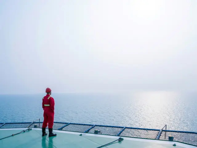 Arbeider i rød verneutstyr står og se ut på havet