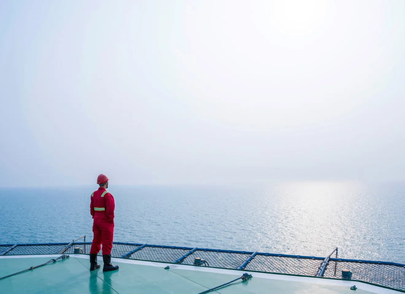 Arbeider i rød verneutstyr står og se ut på havet