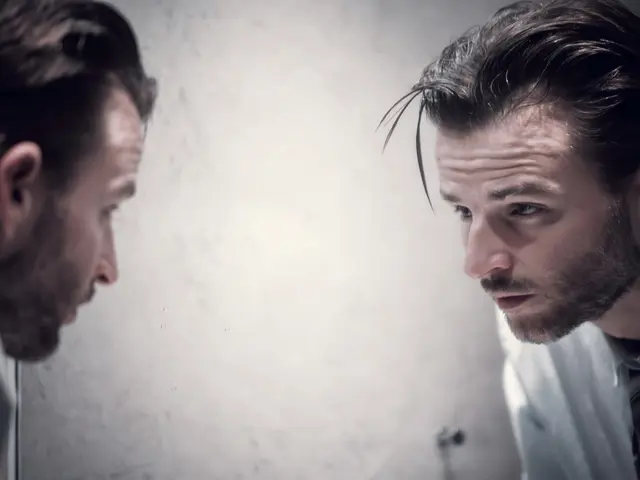 Mann ser seg selv i speilet med et trøtt blikk