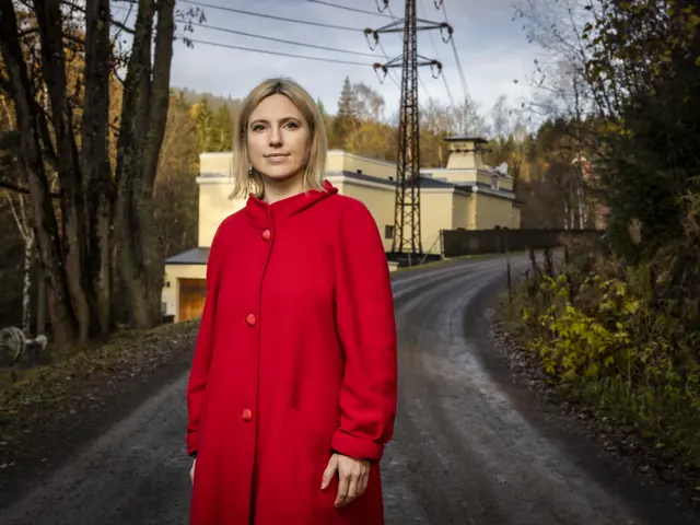 Kvinne i rød jakke ser inn i kamera, hun står utendørs