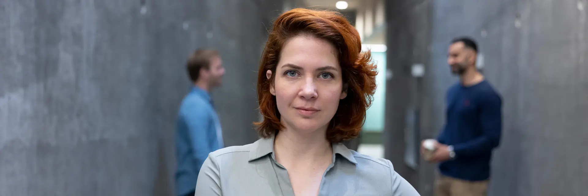 Kvinne ser i kamera, to menn står bak og snakker