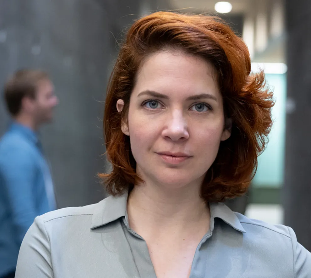 Kvinne ser i kamera, to menn står bak og snakker