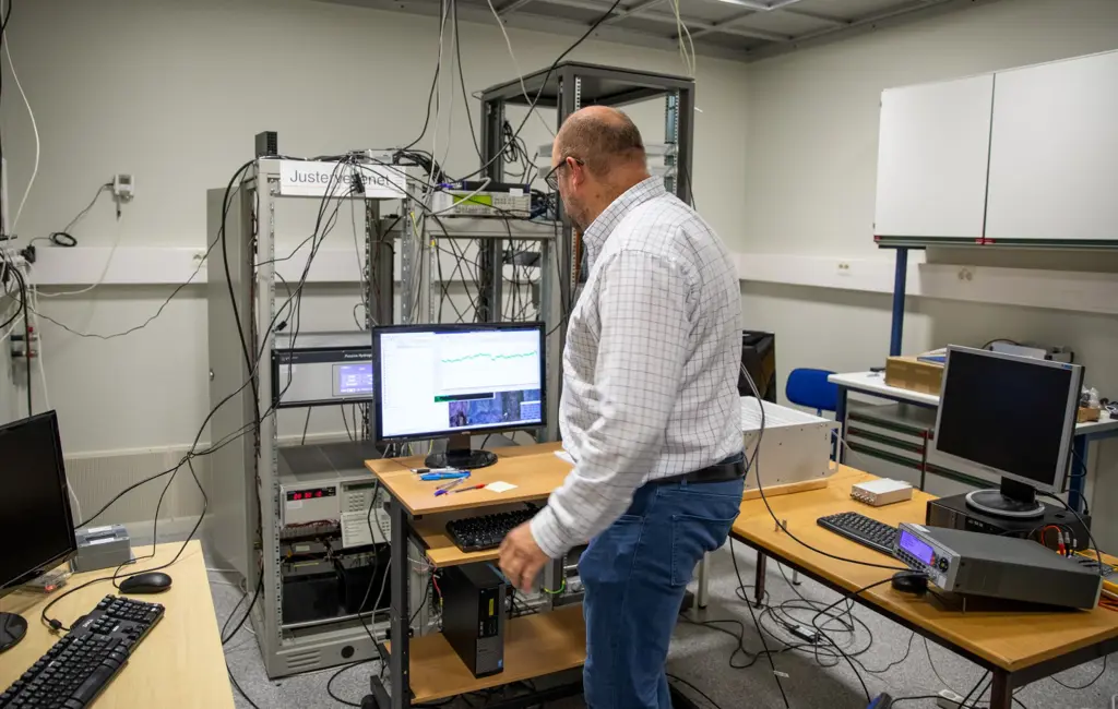 Harald Hauglin står med ryggen til og ser på en dataskjerm i et kontor med masse utstyr