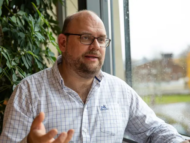 Halvnært bilde av Harald Hauglin som sitter ved siden av et vindu og snakker