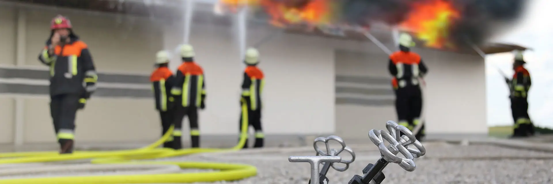 Nærbilde av en brannslage med brannmenn i bakgrunn