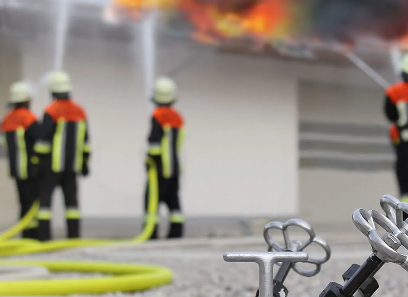 Nærbilde av en brannslage med brannmenn i bakgrunn