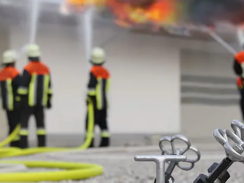 Nærbilde av en brannslage med brannmenn i bakgrunn