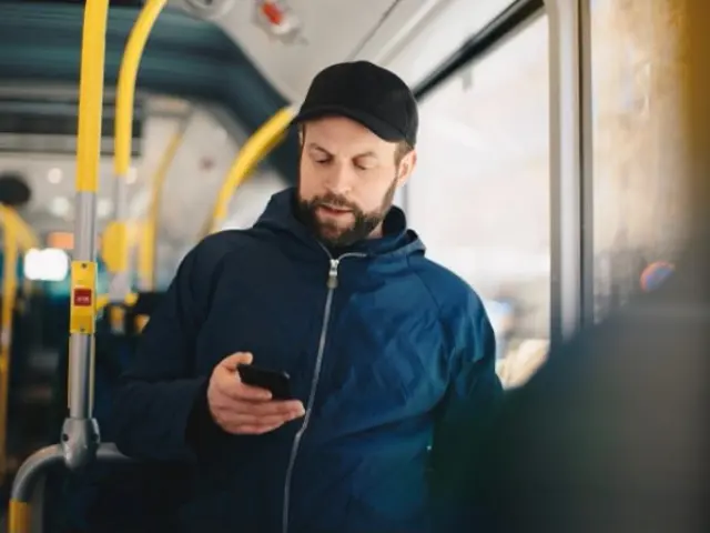 Mann bruker mobil på buss