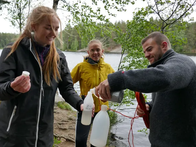 To kvinner og en mann ved vannet fyller vannprøver i flasker