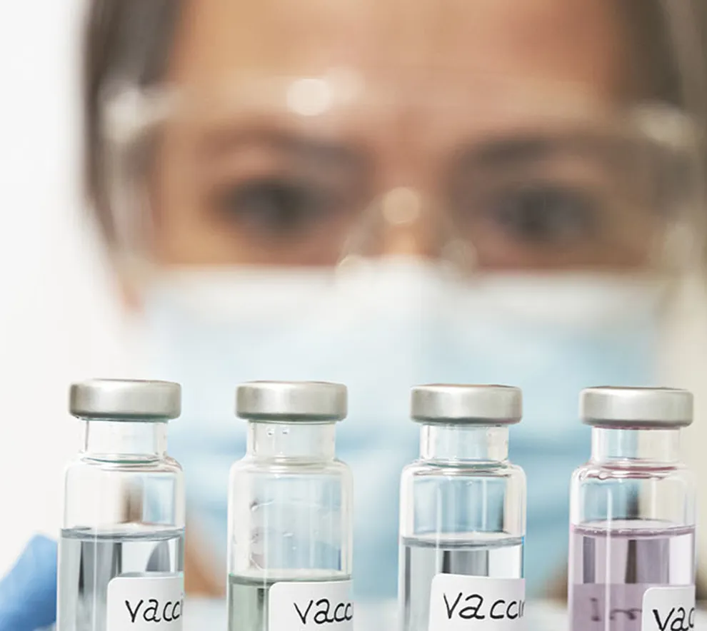 Nærbilde av en kvinne i verneutstyr i labor med reagensglass