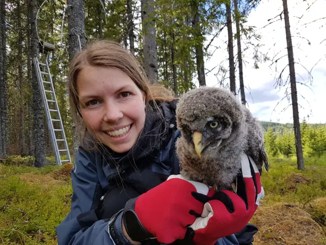 Tina Forsnes i skogen smiler til kamera og holder en ugle