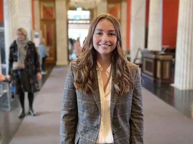 Kvinne står i et stort bygg, smiler mot kamera