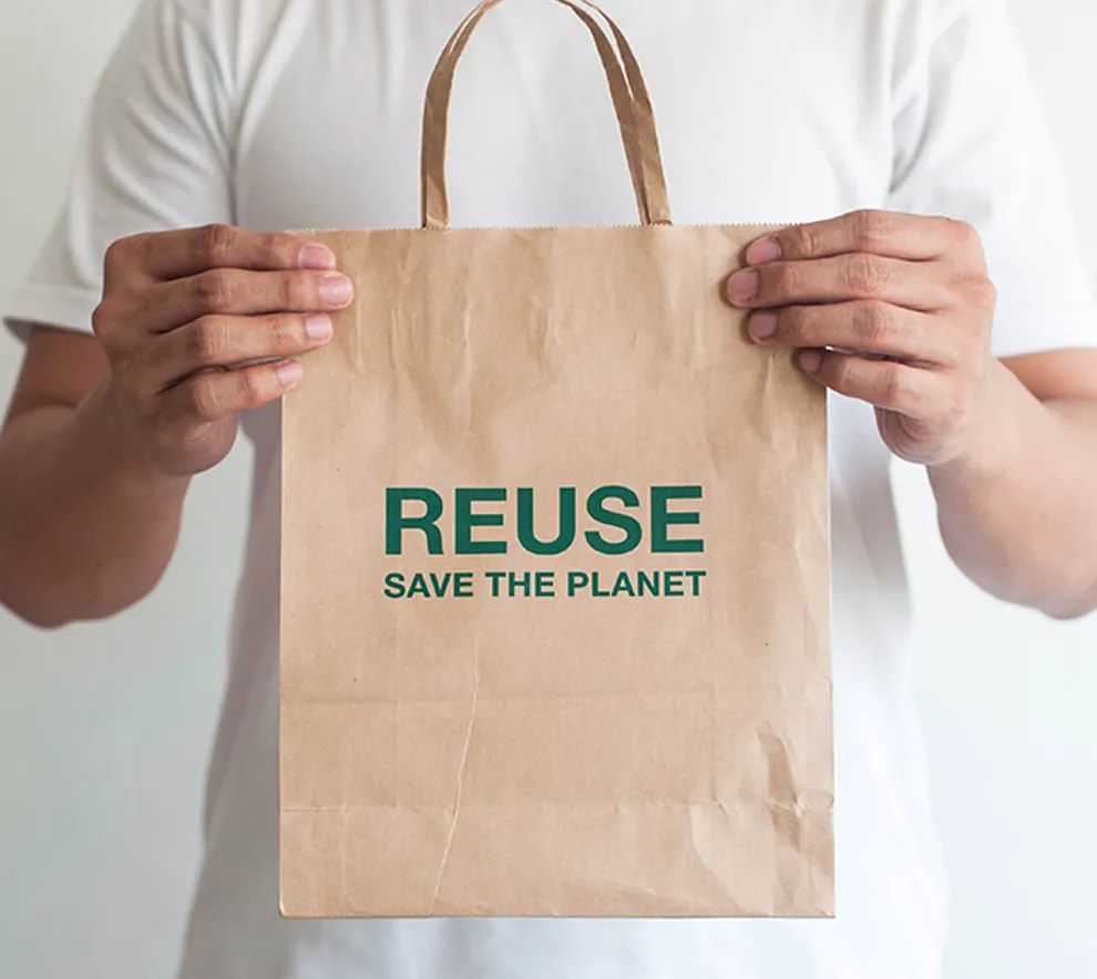 Mann holder papirpose i hendene med skriften Reuse save the planet