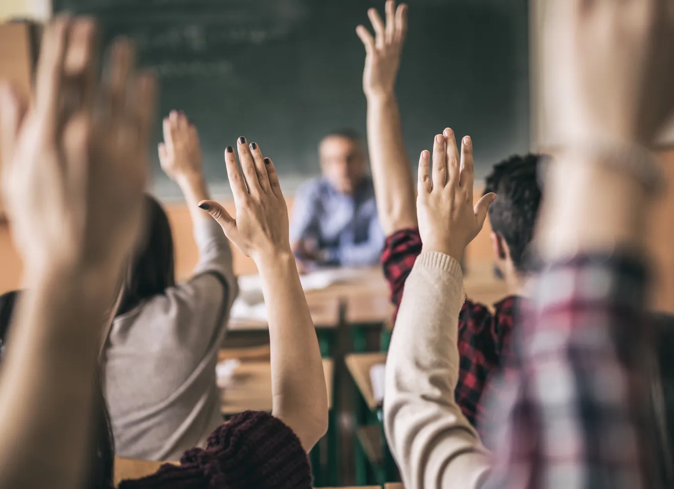 Elever rekker opp hendene i klasserommet