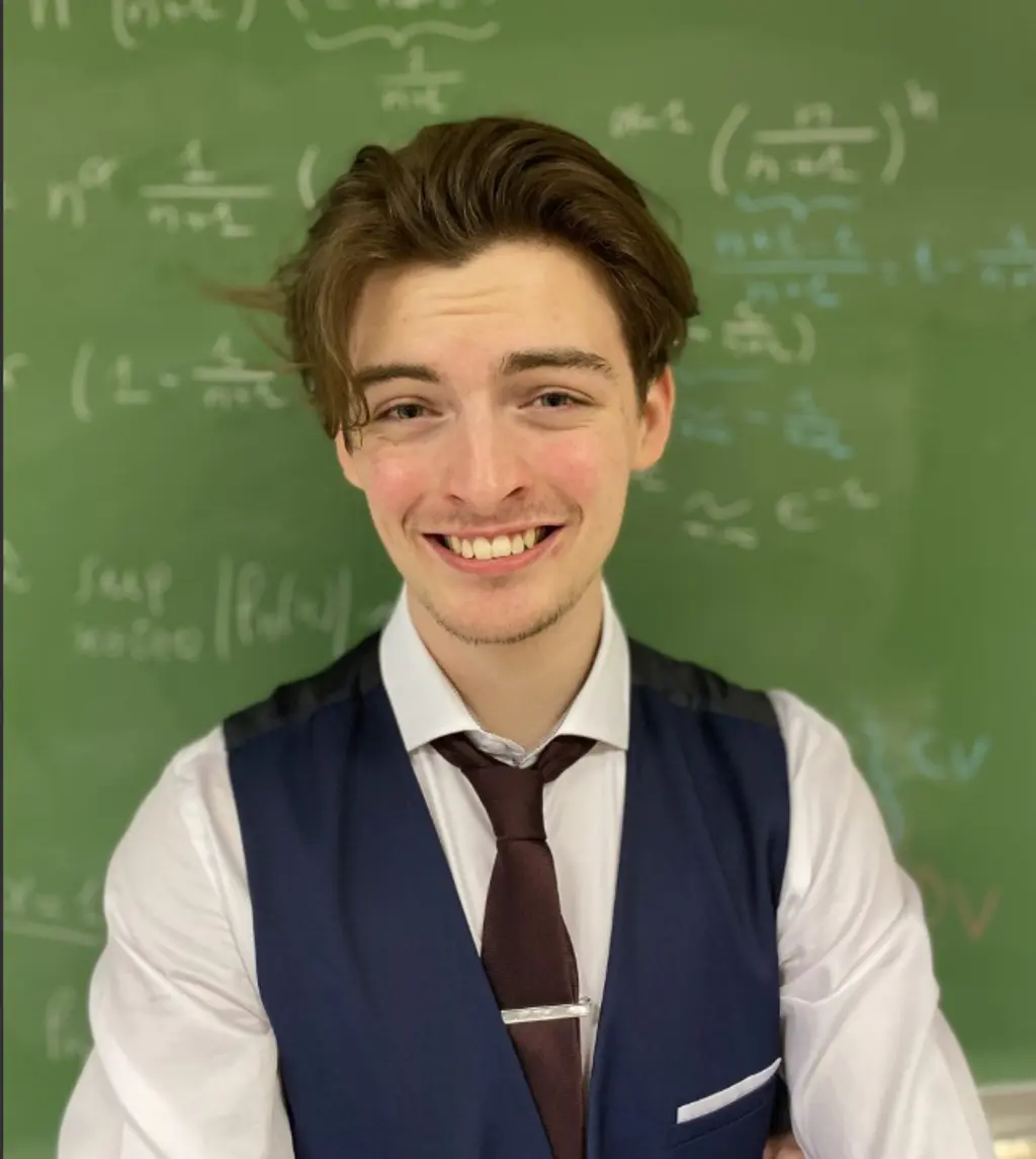 Mann ser inn i kamera, tavle i bakgrunnen