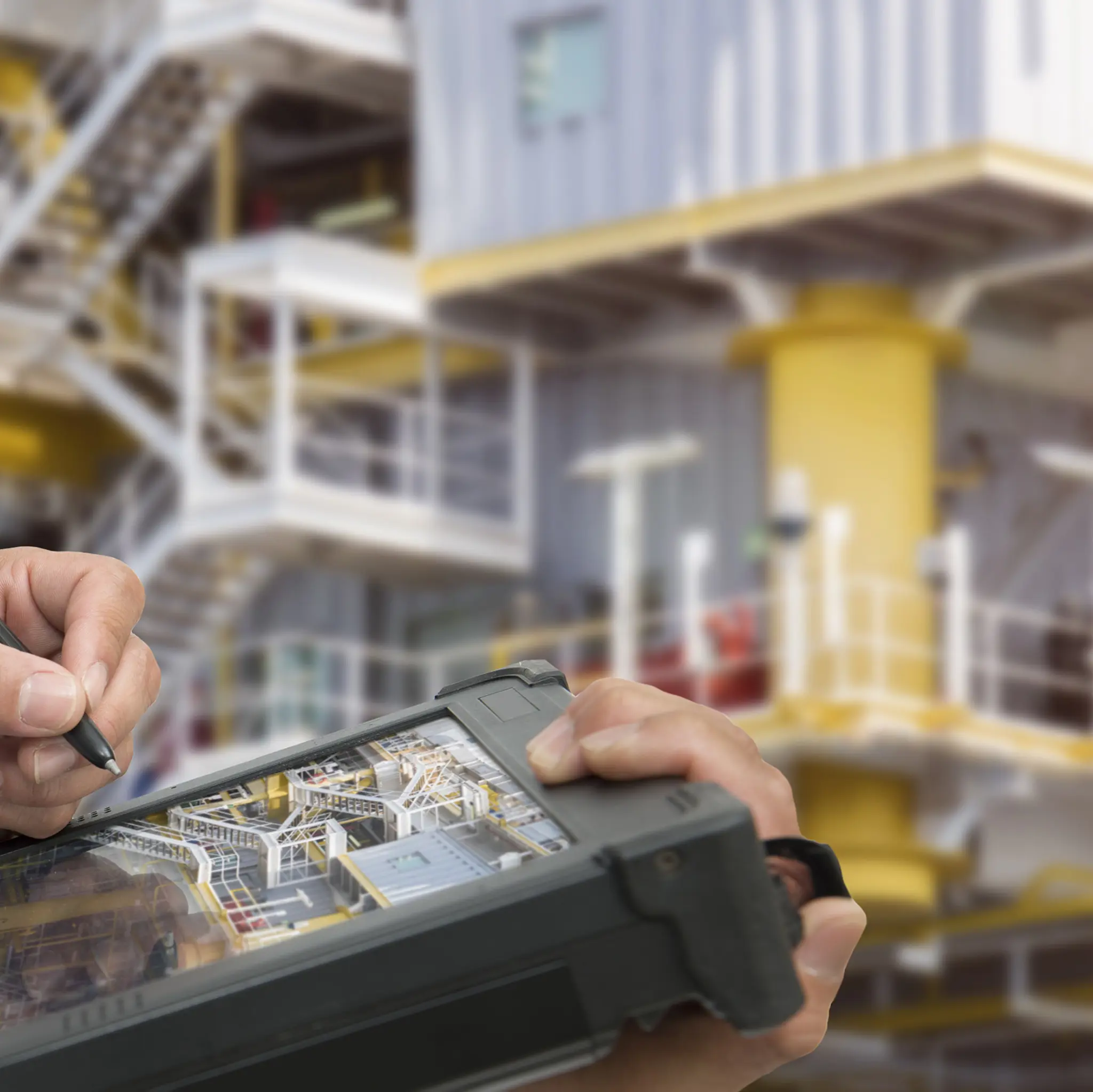 Nærbilde av hender med et nettbrett med en stor oljerigg i bakgrunn