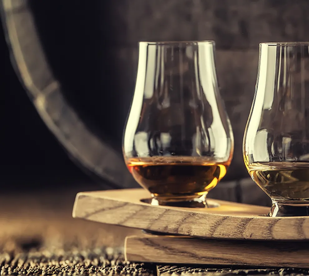 Tre glass med forskjellige typer whiskey foran en tønne