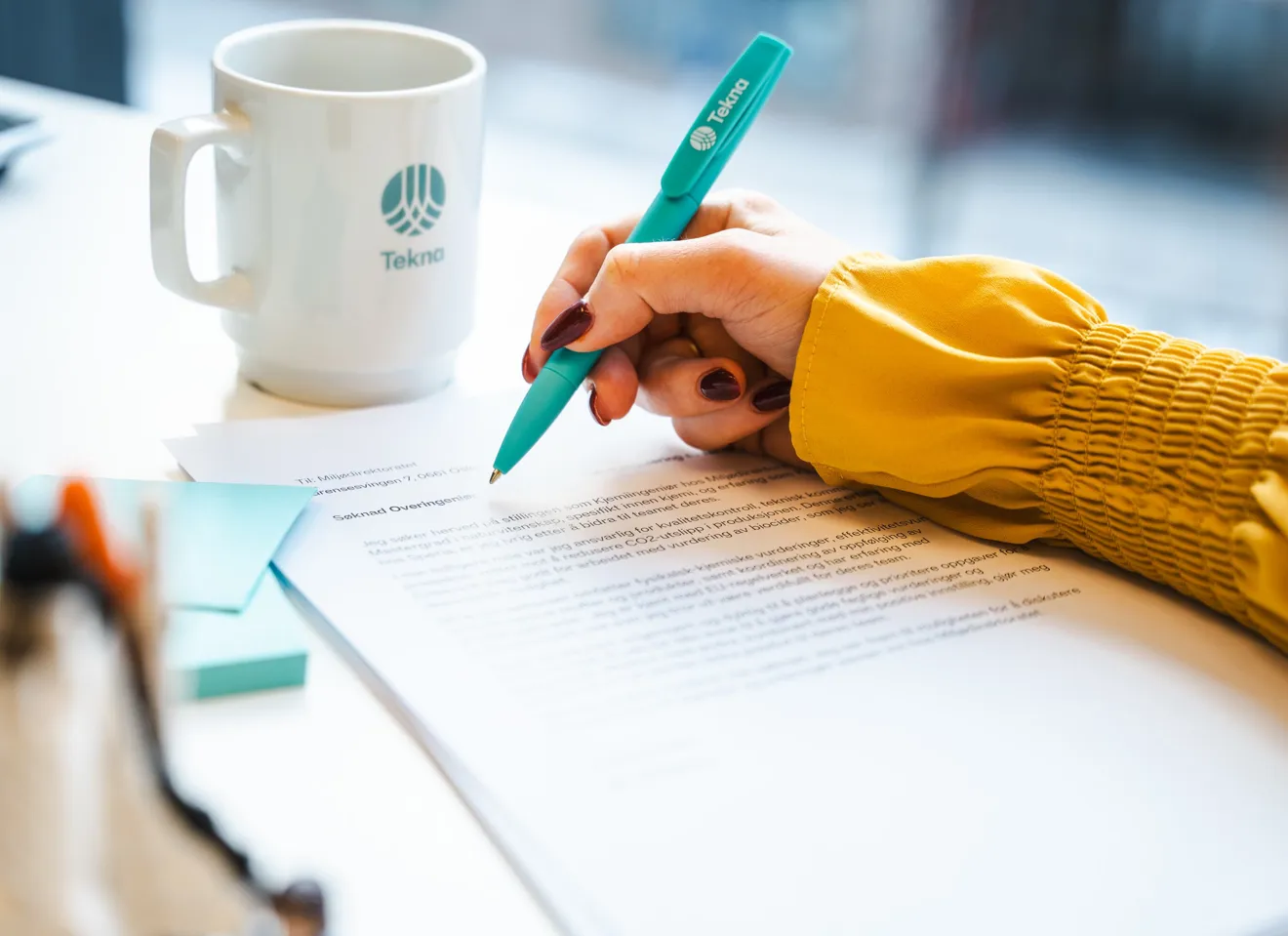Hånd med kulepenn noterer på en utskrevet søknadstekst