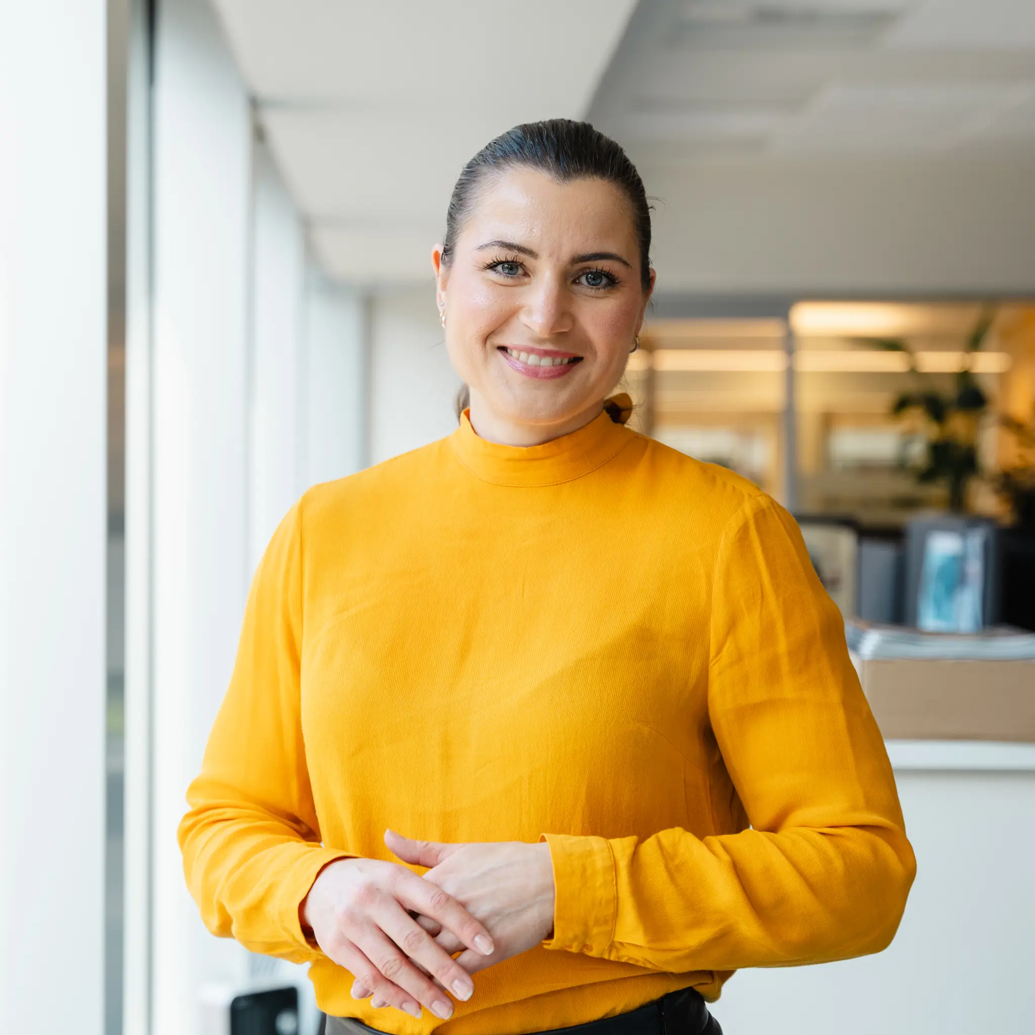 Elisabet Haugsbø smiler, med gul genser, i kontorlandskap
