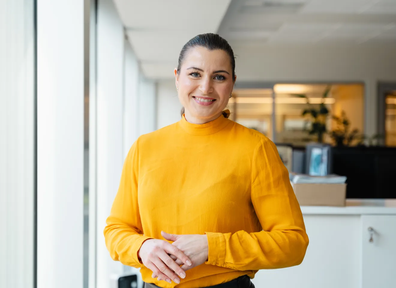 Elisabet Haugsbø smiler, med gul genser, i kontorlandskap