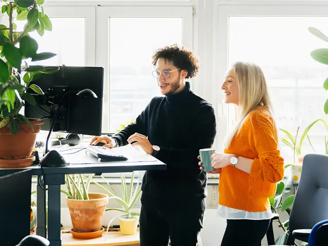 To kolleger i  moderne lokaler med planter jobber ved PC