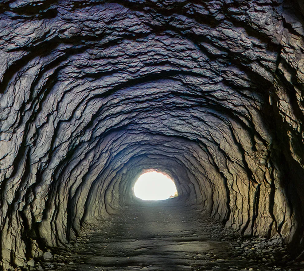 Lang tunnel i fjellet med lys fra åpningen