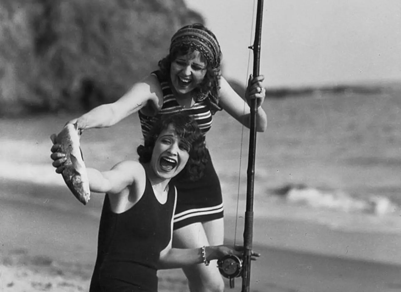 Sort hvit bilde av to kvinner i badedrakt som fisker og har nettopp fanget en fiisk til deres stor glede