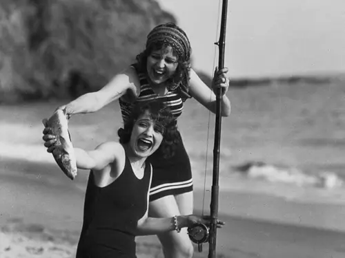 Sort hvit bilde av to kvinner i badedrakt som fisker og har nettopp fanget en fiisk til deres stor glede
