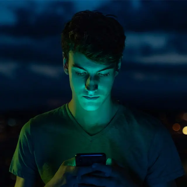 En mann som ser på telefonen utendørs i mørket