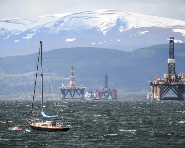 Flere oljeplattformer som blir tauet ut på havet av mange båter