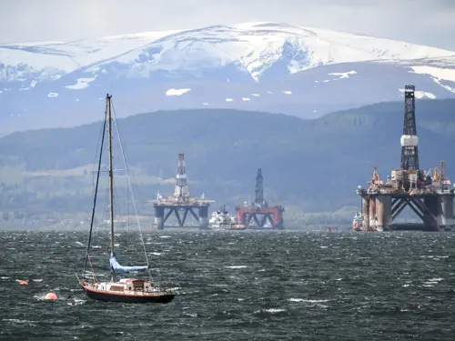 Flere oljeplattformer som blir tauet ut på havet av mange båter